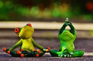 Immagine di due statuine verdi a forma di rana sedute a terra affiancate mentre eseguono posizioni di yoga e meditazione, usata per riferirsi agli interventi psicologici proposto dal Dr. Alessio Congiu per gestire comportamenti impulsivi legati al senso di abbandono