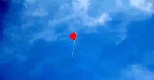 Foto di un palloncino rosso a forma di cuore con un filo bianco pende nel mezzo di un cielo azzurro con nuvole leggere, usata per riferirsi ai problemi di dipendenza affettiva di cui si occupa a Cagliari, Verona e online il Dr. Alessio Congiu