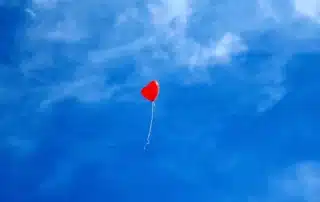 Foto di un palloncino rosso a forma di cuore con un filo bianco pende nel mezzo di un cielo azzurro con nuvole leggere, usata per riferirsi ai problemi di dipendenza affettiva di cui si occupa a Cagliari, Verona e online il Dr. Alessio Congiu